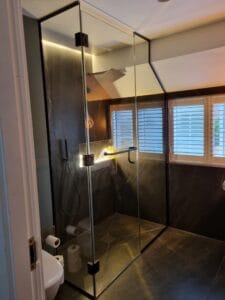 Bespoke glass shower enclosure designed for sloping ceiling loft bathroom in London black fittings