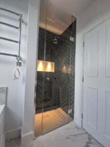 Frameless hinged glass shower door enclosure with chrome fittings installed in London bathroom